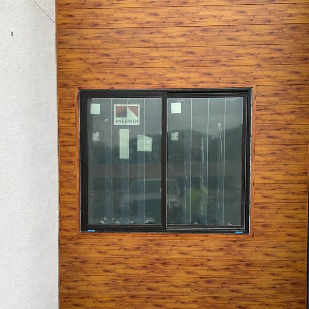 A vertical metal wall with a wood-grain finish with a window.